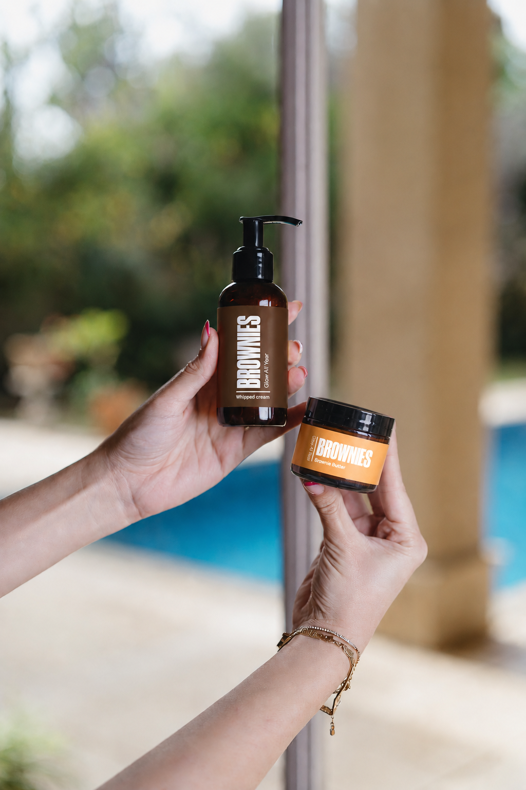Whipped Cream lotion and Brownie Butter balm held by Mediterranean pool
