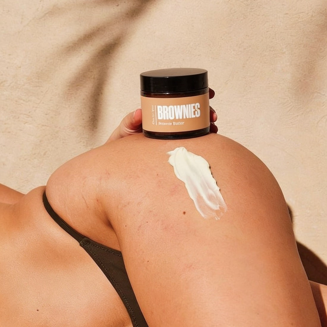 Brownie Butter centella and ginseng cellulite balm held against bronzed thigh