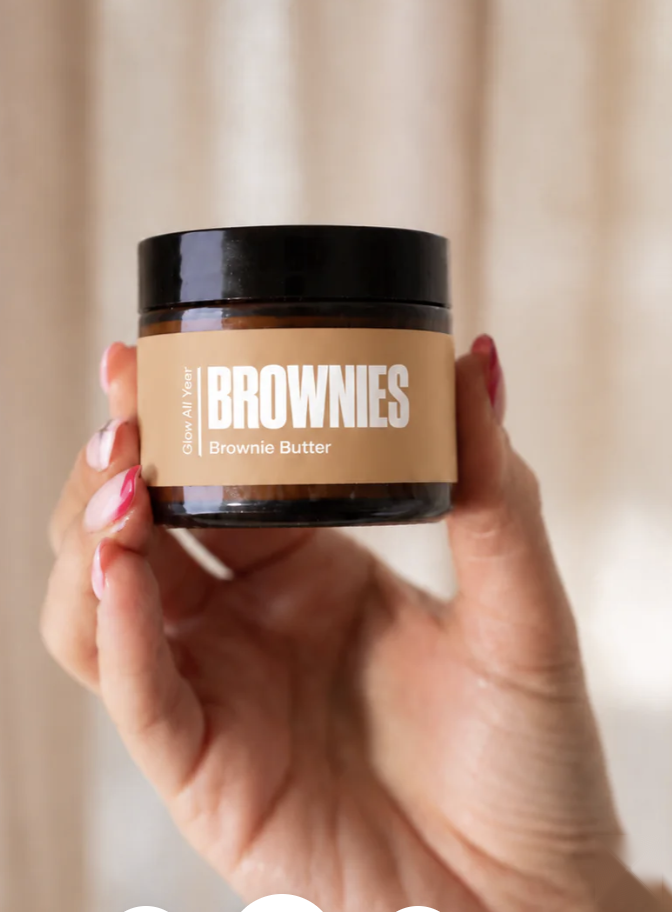Brownie Butter centella and ginseng cellulite balm held against warm linen curtain